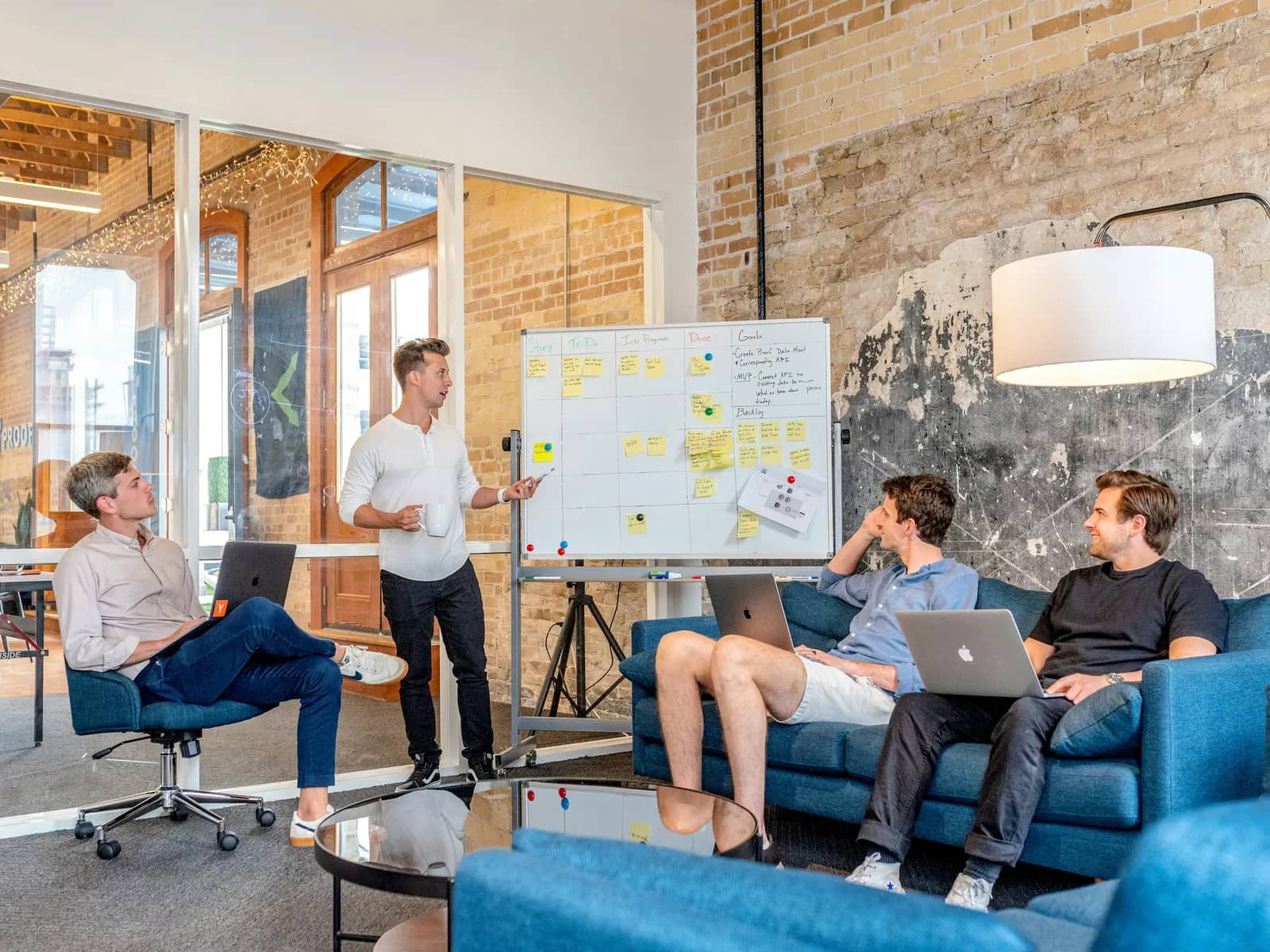 A strategy session in a loft office: one person presents a planning board while the team works on laptops.