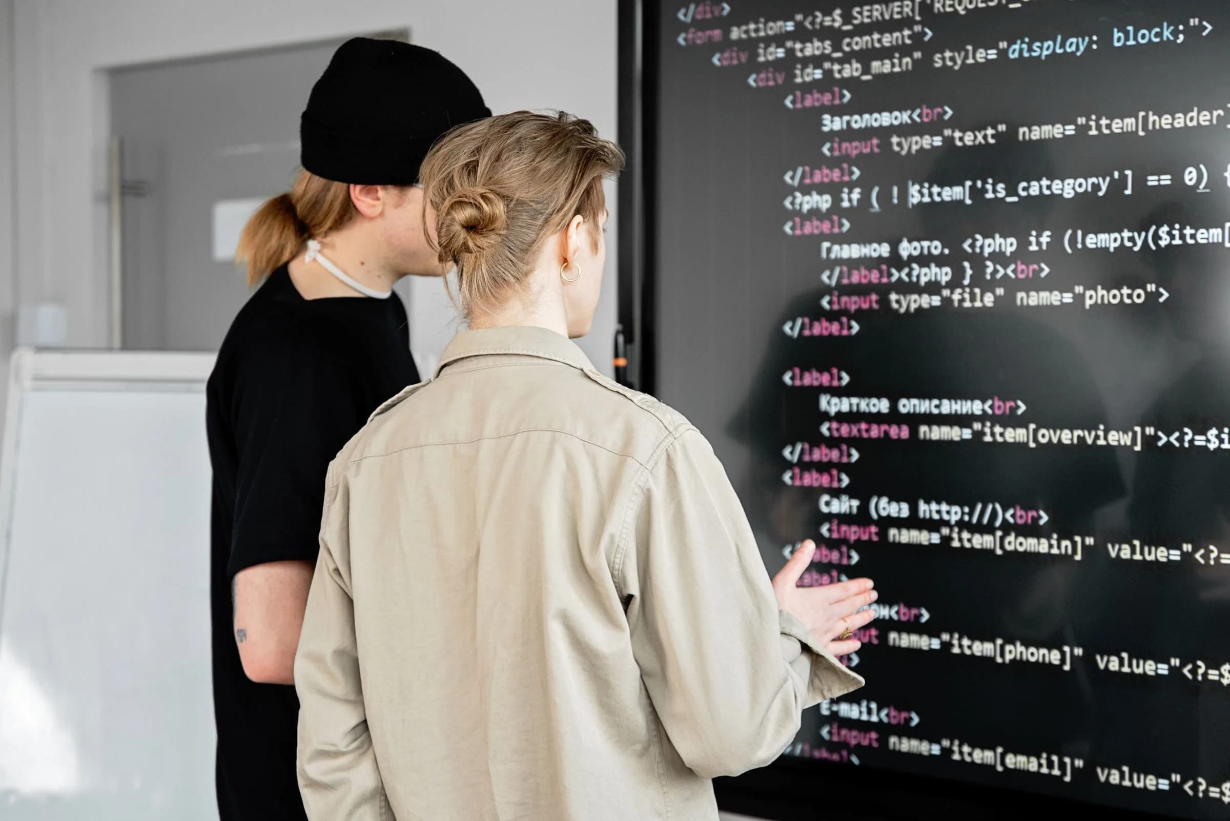 Two people reviewing code displayed on a large wall screen.